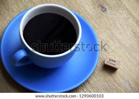 Black coffee in a blue large mug on a blue plate. Next to the cup is a wooden sign saying yes please as coffee is always a good idea