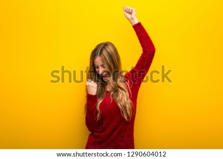 Young girl on vibrant yellow background celebrating a victory