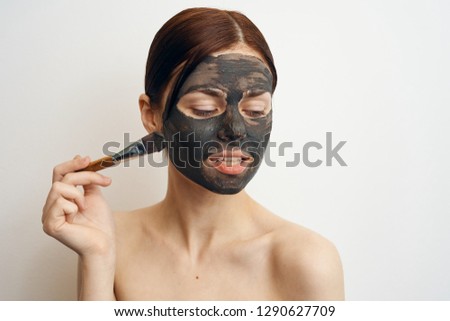 woman applies a clay cosmetic mask on her face with a brush