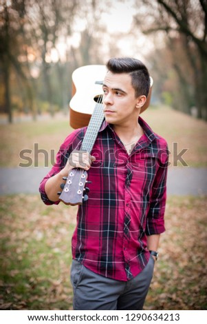Portrait of a  young man with guitar on his shoulder, walinkg on park
