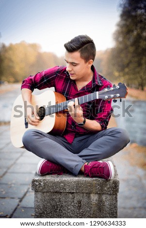 Young man with a guitar in the park, autumn
