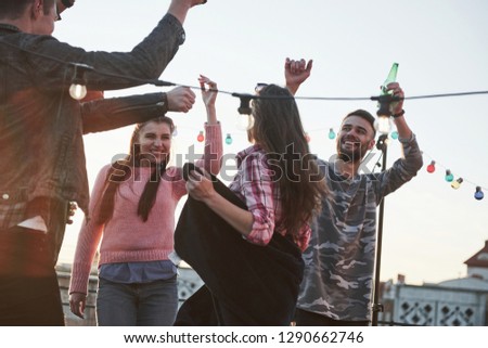Catchy song. You can see it by gestures. Dancing party on the roof with beautiful sunshine at background. Young stylish people.