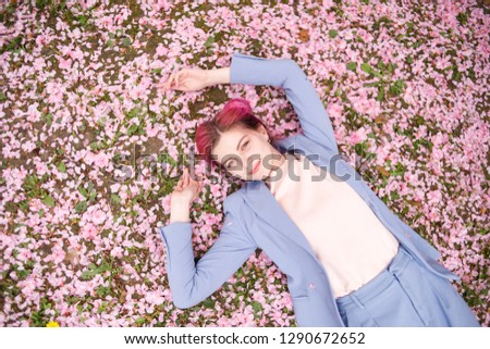 Beautiful young girl in blue suit with pink hair lying on green grass strewn with pink petals