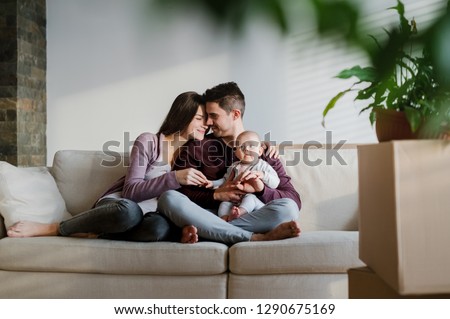 A portrait of young couple with a baby and cardboard boxes moving in a new home. Royalty-Free Stock Photo #1290675169
