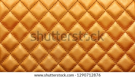 Close-up texture of genuine leather with rhombic stitching. Rich gold color. Luxury background