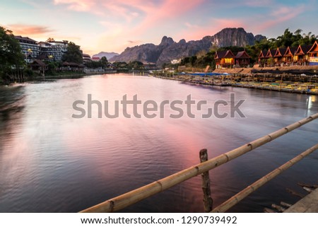 Wooden bridge walkway cross over the river at sunrise or sunset with mountain background at Vang Vieng , Laos