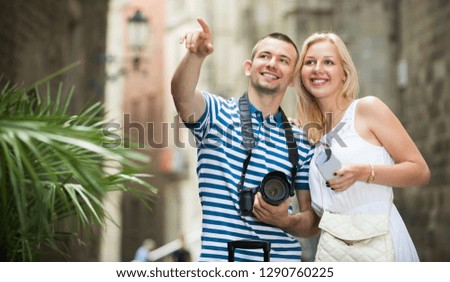 Smiling man and woman tourists taking camera in hands and photographing in city
