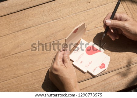 Top view. Hand of old woman writing a card on Saint Valentines Day, Valentines day card concept, Wooden background, 