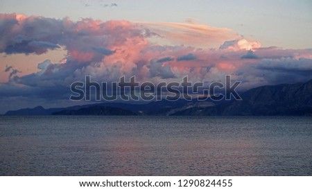            Clouds are streaky salmon pink as the sun sets over the coastal mountains of Crete, Greece                   