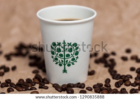 Paper glass with a picture and a drink. Coffee beans lie side by side on the table.