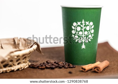 Paper glass with a picture and a drink. Coffee beans, cinnamon and glazed sweets are next to each other on the table. Brown tones in the photo.