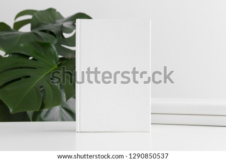 White book mockup with workspace accessories and a monstera plant.
