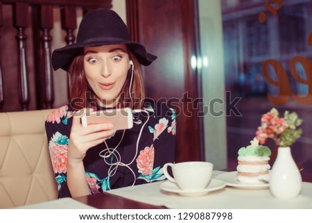 Front view of a fashion girl amazed shocked woman checking smart phone in coffee shop face looking at cellphone towards camera. Girl received shocking good news or amazing deals online in social media