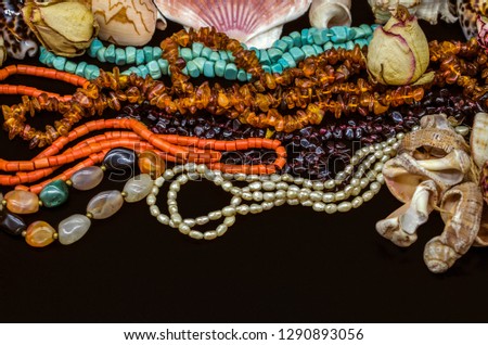 Bright old beads of turquoise, red coral, amber, pomegranate, colorful agate, pearls among dry buds and seashells on a black background



