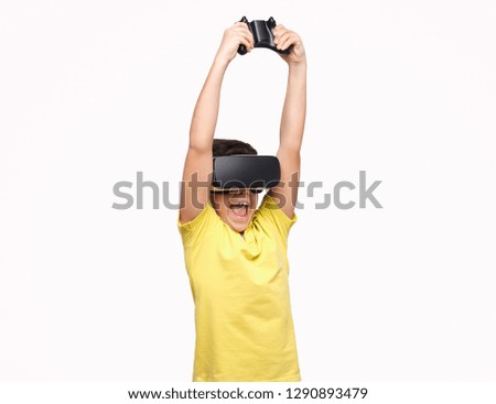 Excited boy in VR goggles screaming and holding controller over head while standing on white background and playing video games