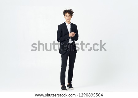 Curly business man standing in a dark suit in full growth on a light background