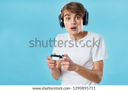 The guy with the controller from the console in his hands and in the headphones plays games on a blue background