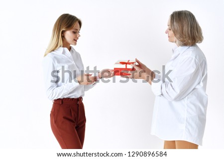 An elderly woman and granddaughter hold a gift box in white shirts on a light background