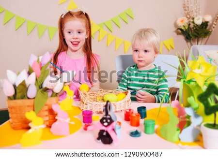 happy Easter - a little girl with red hair and a blond boy preparing for the Easter celebration and painting eggs for the Easter basket