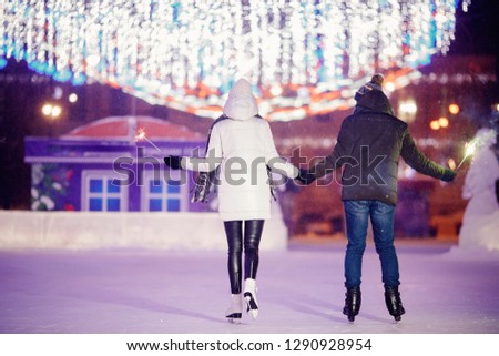 Winter skates, loving couple holding hands and rolling on rink. Illumination in background, night. Concept training. Back view.