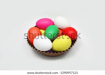 Multi colored easter eggs in a brown basket against a white background. 