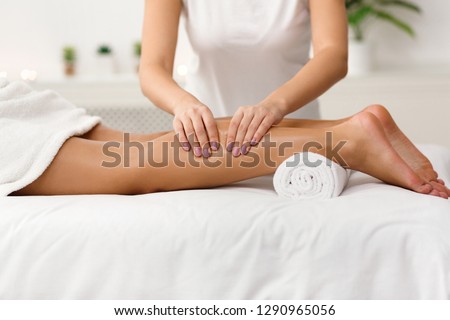 Massage therapist massaging woman calves in spa center, side view