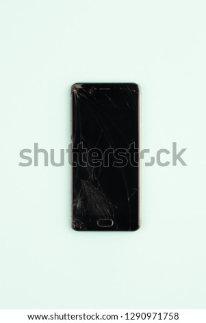 Mobile phone with broken black screen, top view. Distressed damaged smartphone in pale green background, vertical shot