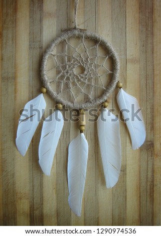 Dream catcher, decorated with white feathers and wooden beads, on a wooden surface.