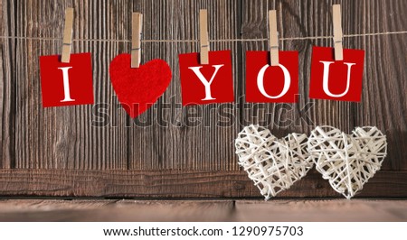 Clothes pegs and I LOVE YOU words on papers on rope on wooden background with wicker hearts Valentines day concept