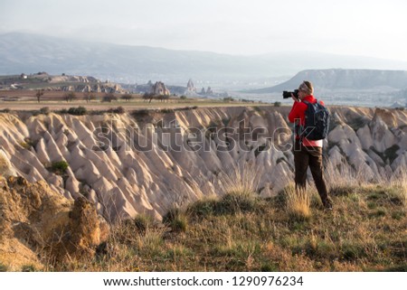 Amazing day in Cappadocia mountains, Turkey. Photographer in red jacket taking photo of amazing hills. Landscape photography