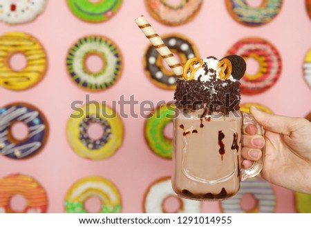 Woman holding mason jar of tasty milk shake with sweets near decorated wall, closeup. Space for text