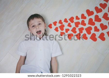One little boy lying on the floor. Near lying paper hearts, it is a inspirational message. Concept of happy Valentine day.