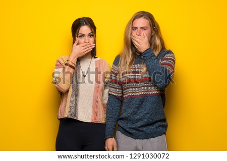 Hippie couple over yellow background covering mouth with hands for saying something inappropriate