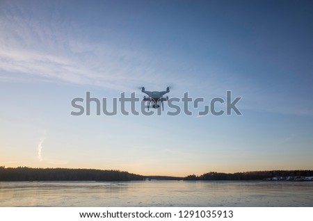 White drone flying in air over ice lake in Sweden Scandinavia Europe on cold winter evening. Nice outdoors at sunset. Nature, landscape and blue sky.
