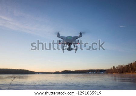 White drone flying in air over ice lake in Sweden Scandinavia Europe on cold winter evening. Nice outdoors at sunset. Nature, landscape and blue sky.
