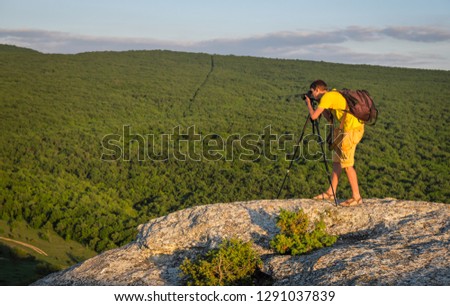 Photographer with tripod and backpack on the rock in the evening.