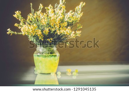 Bouquet of bright yellow wildflowers in transparent vase on glass table. Hydrogel in jar for decor. Copy space. Warm summer or spring background