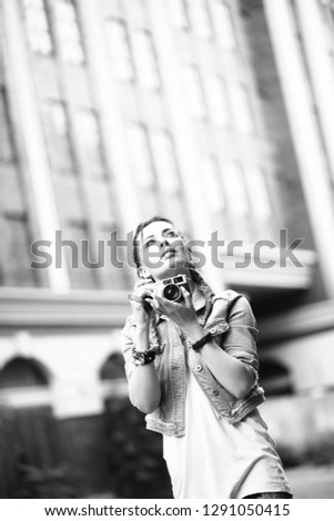 Attractive young brunette girl walks through the city streets and takes pictures with a retro camera. Black and white image.