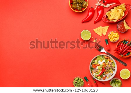 Set of traditional mexican dishes - burrito bowl, nachos, guacamole and salsa dressing, chili peppers, chopped jalapeño and lime on red background. Overhead view, flat lay, copy space Royalty-Free Stock Photo #1291063123