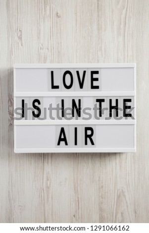 Modern board with text 'Love is in the air' on a white wooden background. Valentine's Day 14 February.