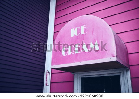 Pink and purple Ice Cream building with faded sign and white text. 
