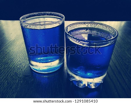 Tasty transparent soda drinks. Drinks have a blue color. Unhealthy soda drinks containing lots of sugar. Both glasses are full. The background is dark blue.