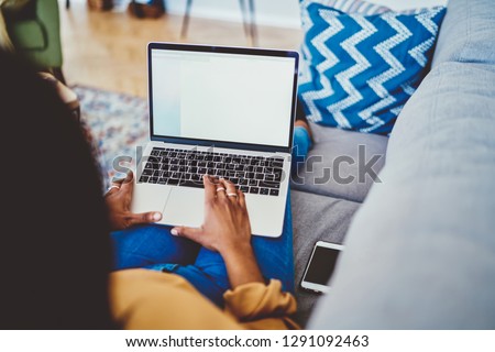 Cropped image of dark skinned woman typing on laptop computer with mock uo screen spending time at home interior, female freelancer working remotely lying on sofa with modern netbook connected to wifi