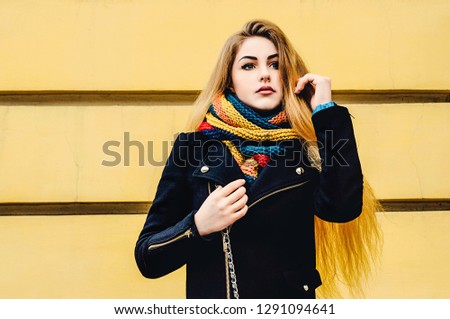 Young beautiful blonde against the yellow wall in winter clothes stands and dreams. Winter portrait.