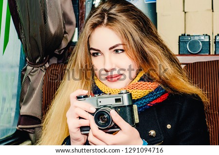 Young beautiful blonde woman with a vintage camera takes pictures in a cafe. Winter portraits of the photographer.