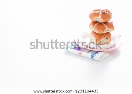 Hot cross buns on a pink plate, next to a flower. Everything on the white, Easter table.