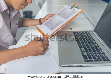 Side view of Asian businessman holding financial report and writing note