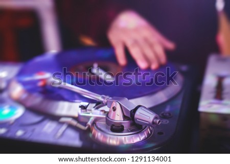 View of Dj mixer and vinyl plate with headphones on a table with DJ playing and mixes the track in the background, during night techno party in the nightclub