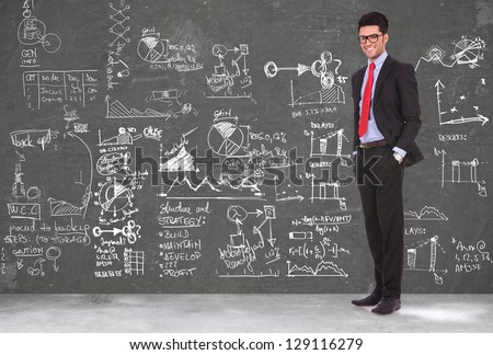 full length picture of a young business man standing with hands in pockets in front of a blackboard full of sketches and charts
