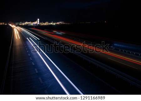 Night urban scene of motion blurred light tracks glowing to the darkness of highway traffic transport to the city just after sunset. Creative long time exposure diagonal composed photography.